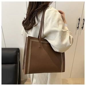 Close-up of brown pebbled leather tote bag with white stitching and brand text details
