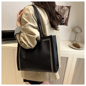 Close-up of a large black leather tote bag with elegant white contrast stitching details