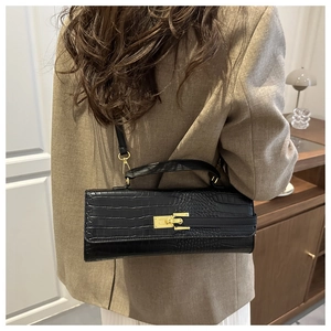 Detail of black crocodile texture handbag with gold buckle shown on person