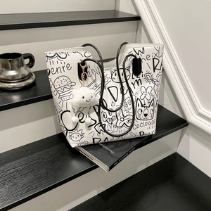 White graffiti tote bag with black cartoon patterns and plush charm on black steps