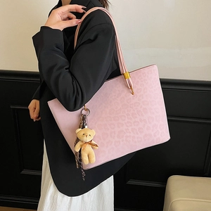 Pink leopard print tote bag with plush bear charm and gold hardware shown on a shoulder