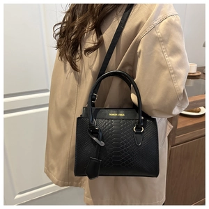 Detail of black faux-crocodile pattern handbag with gold fashion text and round handle