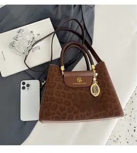 Détail d'un sac à main léopard avec anse en cuir tressé et pendentif feuille
