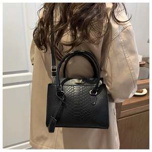 Detail of black textured leather bag with gold lettering shown on a model's shoulder