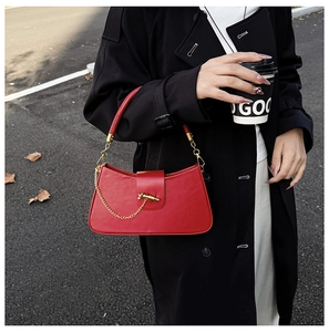 Detail of red leather baguette bag with gold chain strap held by a model in black coat
