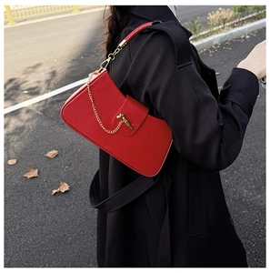 Detail of red leather baguette bag with gold chain and metal lock on a black coat