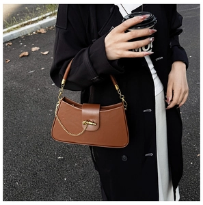 Detail of brown matte leather saddle bag featuring gold chain and metallic twist lock clasp