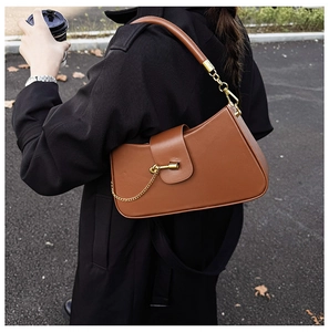 Detail of brown half-moon leather shoulder bag with golden knot clasp and high-end texture
