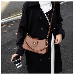 Detail of high-quality brown crossbody saddle bag with gold metal buckle and chain strap