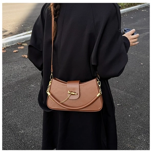 Rear view of brown leather crossbody bag with chain and gold clasp on a model in a coat