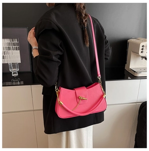 Detail of bright pink leather saddle bag with gold chain and twist lock on a shoulder strap