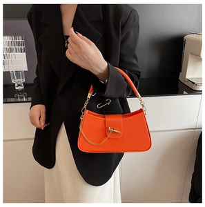 Chic orange leather handbag with gold chain detail and metal bar lock on a model