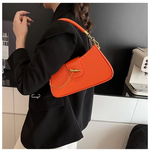 Detail of bright orange crossbody saddle bag with gold metal chain on black blazer