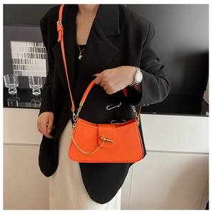 Close-up of orange leather crossbody bag with iconic gold chain and toggle closure detail