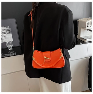 Detail view of bright orange leather crossbody bag with gold chain and hardware lock