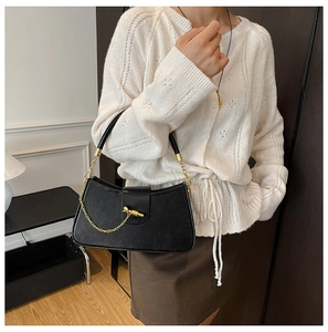 Detail of elegant black matte leather bag featuring gold chain and unique metal clasp