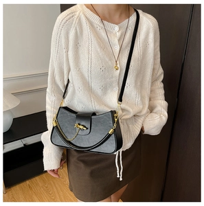 Detail of a black crescent shoulder bag with golden twist lock and decorative chain