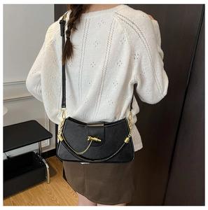 Detail of black crossbody box bag with gold chain handle and adjustable strap on a model