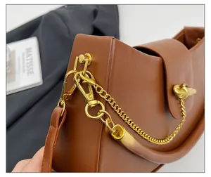 Detail of brown leather saddle bag featuring a gold chain and twisted knot metal lock
