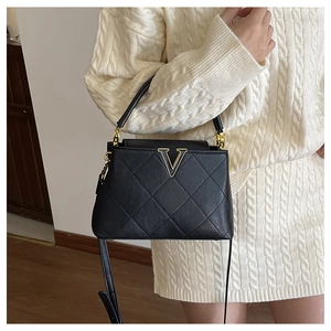 Detail of black quilted leather bucket bag with gold V hardware held by model in white sweater