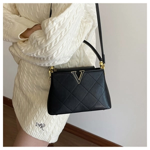 Detail view of black quilted leather shoulder bag with golden V-buckle on a knit dress