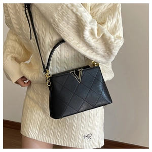 Detail shot of black quilted shoulder bag with gold V logo on white knit dress