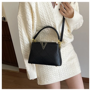 Detail of black quilted leather handbag with gold V-shape twist lock and chain strap