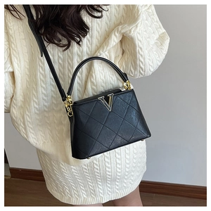 Detail of black quilted leather bucket bag with gold V-hardware worn by model