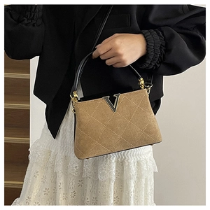 Detail of tan quilted suede handbag featuring a gold V-shaped logo and black leather handle