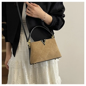 Detailed close-up of brown suede bag with quilted pattern and gold V-shaped logo
