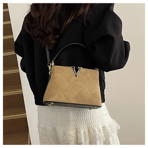 Detail view of brown quilted matte handbag with golden V-shaped metal hardware accessory