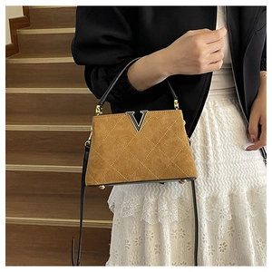 Detail of a brown quilted bucket bag featuring a gold V-shaped metal twist-lock clasp