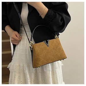 Detail of tan suede bucket bag with quilted diamond pattern and metallic V-shaped buckle
