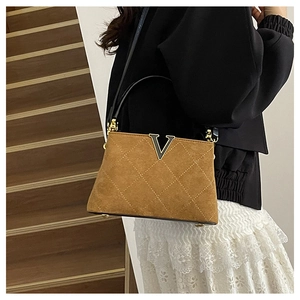 Detailed view of brown quilted suede bucket bag with metallic V buckle and black top handle