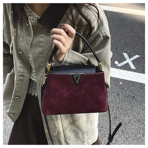 Detail of burgundy quilted suede bucket bag with gold V logo held by a model