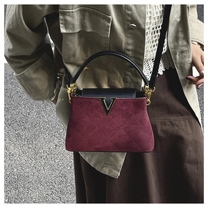 Macro detail of wine red suede bag featuring diamond stitching and gold V-shaped buckle