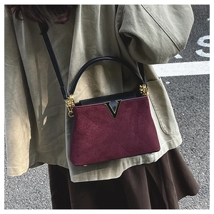Close-up of quilted burgundy suede handbag with gold V-metal decor and black leather handle