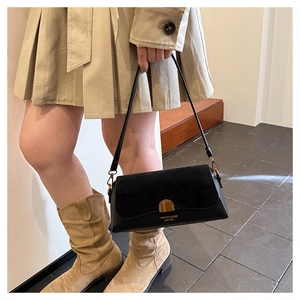 Detail of a chic black leather baguette bag with a gold buckle worn in a street style look