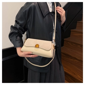 Detail of cream baguette bag with suede flap and gold buckle on a black leather jacket