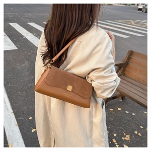 Detail view of caramel brown baguette bag with leather stitching on a wooden bench