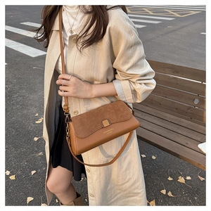 Close-up of a brown patchwork baguette bag styled with a beige trench coat on a city street
