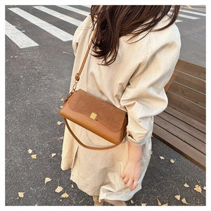 Detail of caramel patchwork leather handbag with gold buckle on autumn park bench