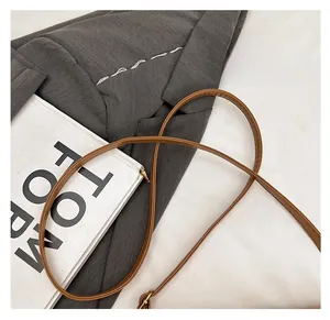 Detail showing brown leather shoulder strap with gold buckle on gray suit background