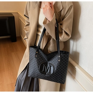 Détail du sac cabas noir à motif lettres M porté à l'épaule par un mannequin