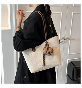 Detail of off-white tote bag with litchi texture and leopard pom-pom accessory
