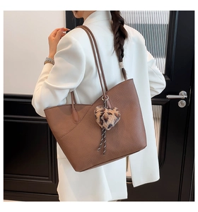 Close-up of brown litchi pattern tote bag with leopard heart plush charm on model