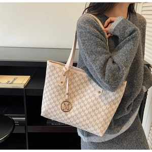 Detail of cream tote bag with brown monogram M pattern and elegant gold pendant charm