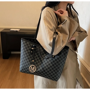 Model wearing large tote bag with M-letter print and round metal charm detail
