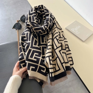 Detail of knit scarf featuring black and beige geometric patterns and soft fringed edges