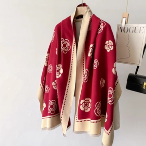 Detail of red and cream cashmere scarf featuring camellia patterns and fringe hanging on a rack